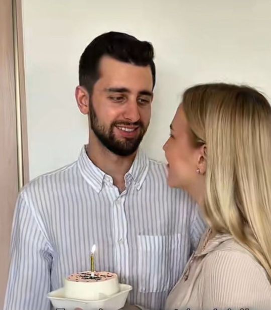 парень и девушка смотрят друг на друга счастливыми глазами и улыбкой на лицах. В руках держат тортик с одной свечой которая говорит об их первой годовщине :)